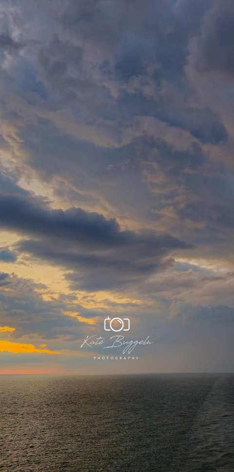 Moody ocean sunset beneath dramatic storm clouds captured by Kate Buggeln Photography.